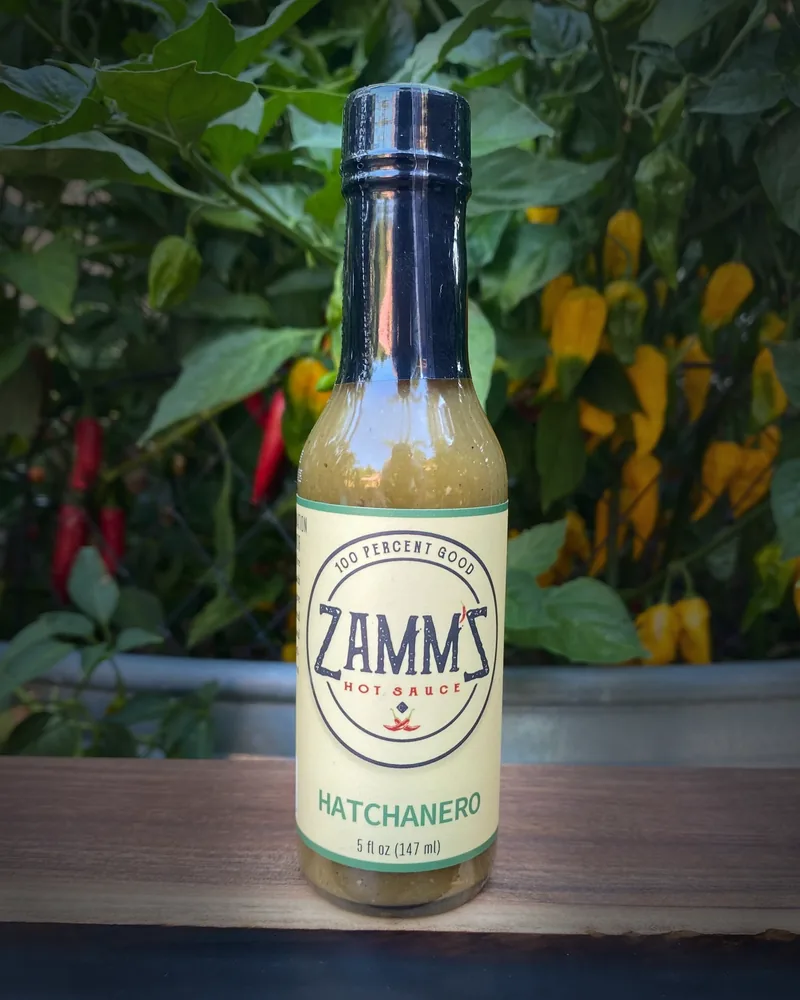 A bottle of Zamm'Z Hatchanero hot sauce among peppers